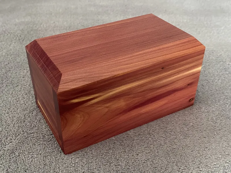 A cedar wood slide urn with warm red and amber grain, resting on a grey surface